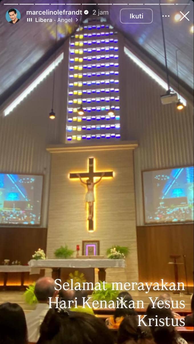 Umat menghadiri misa di dalam gereja dengan salib bercahaya dan jendela kaca berwarna untuk memperingati Hari Kenaikan Yesus Kristus.