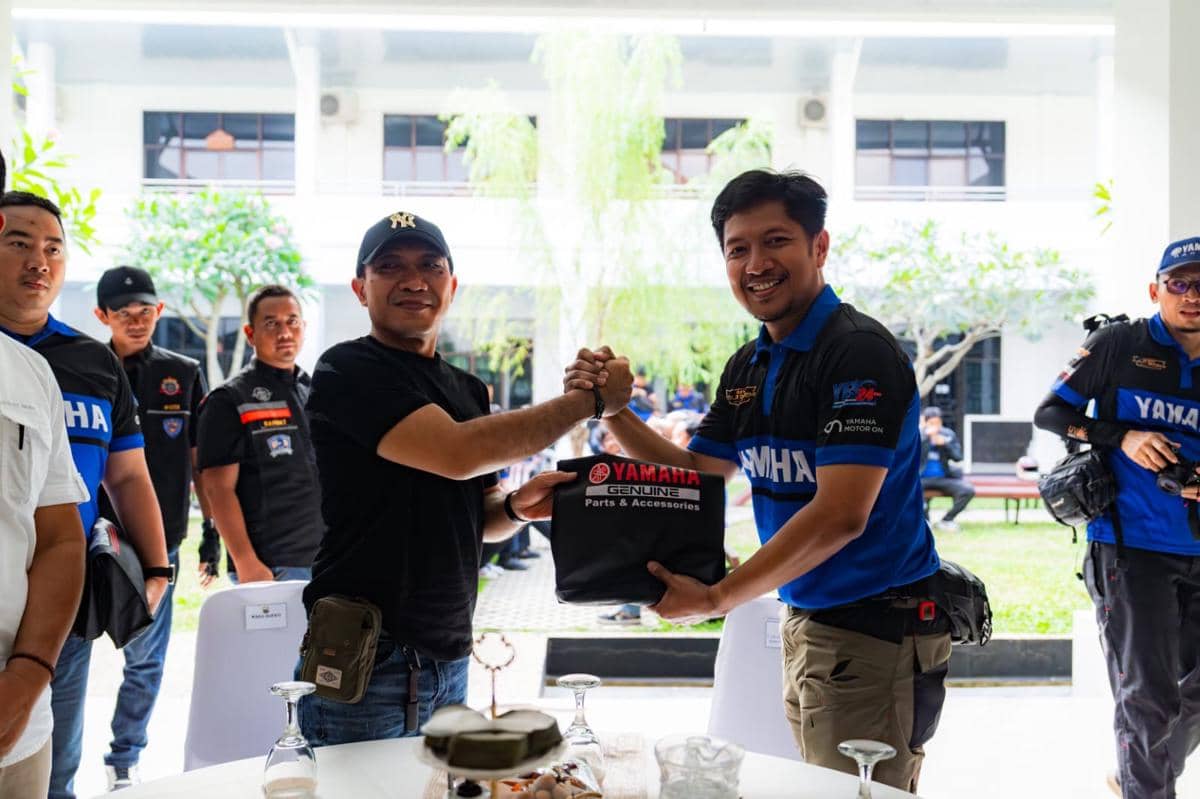 Dua pria berjabat tangan sambil menyerahkan paket bertuliskan Yamaha Genuine Parts & Accessories di acara komunitas motor.