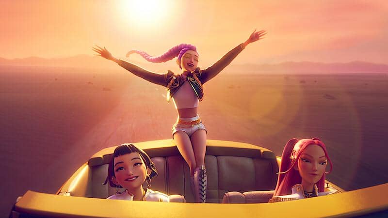 Tiga karakter animasi perempuan dari film KPop Demon Hunters menikmati perjalanan di mobil terbuka saat matahari terbenam di gurun.