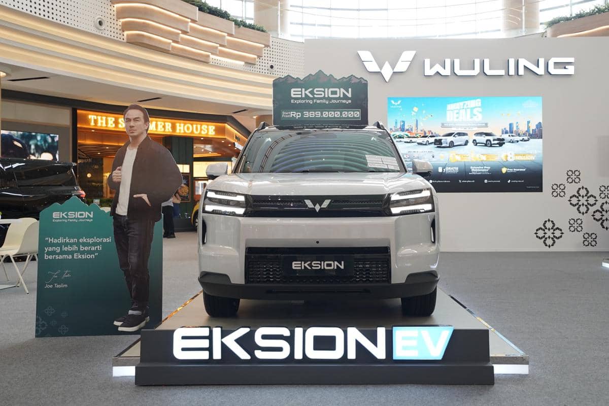 Mobil listrik Wuling Eksion EV berwarna putih dipamerkan di area pameran dalam ruangan dengan latar logo Wuling dan papan harga.