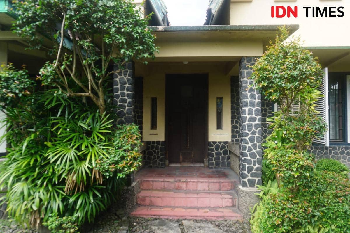 Tampak depan rumah peninggalan Prof. dr. M. Sardjito di Kelurahan Terban, Yogyakarta, dengan dinding batu alam dan tanaman hijau di sekitarnya.