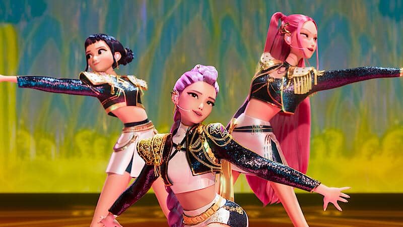 Tiga karakter animasi perempuan dengan kostum panggung glamor menari di atas panggung berwarna cerah dalam film KPop Demon Hunters.