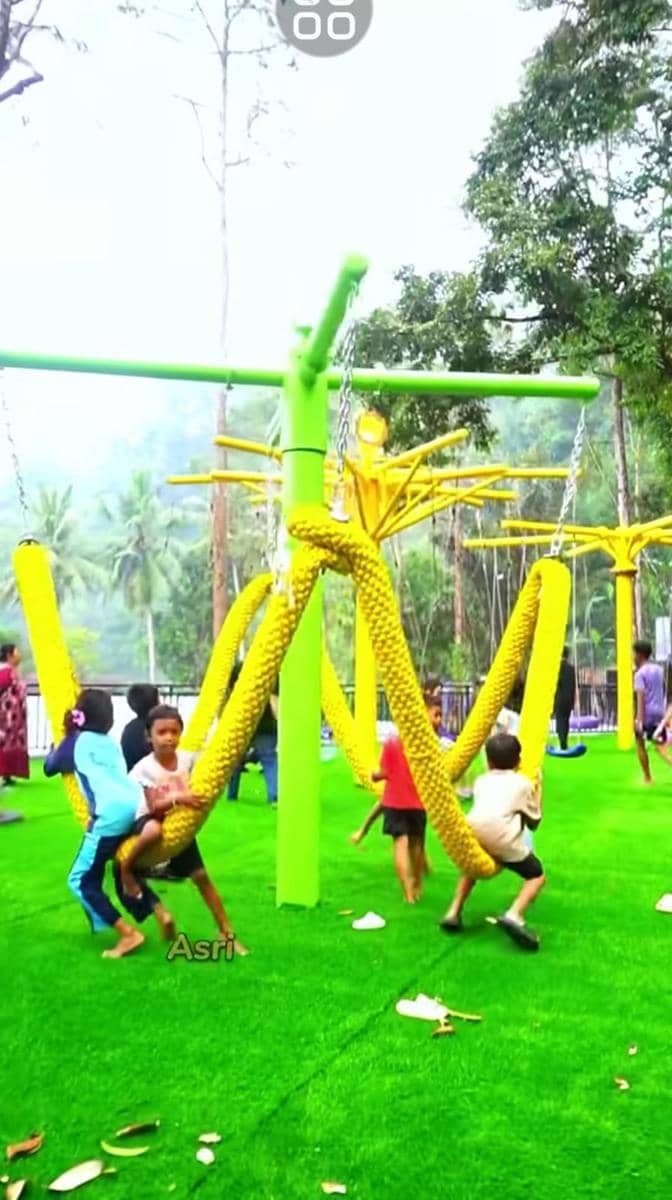 Anak-anak bermain di area permainan dengan ayunan tali berwarna kuning di The Nice Park Lampung yang dikelilingi pepohonan hijau.