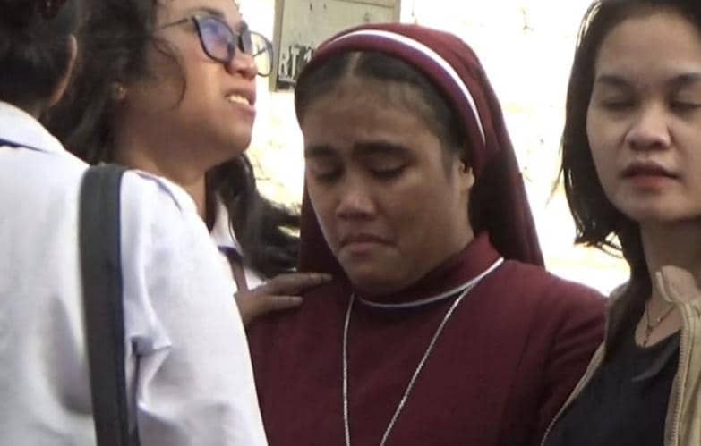 Seorang suster mengenakan pakaian biara berwarna marun tampak sedih dan ditenangkan oleh beberapa wanita setelah kebakaran panti asuhan.
