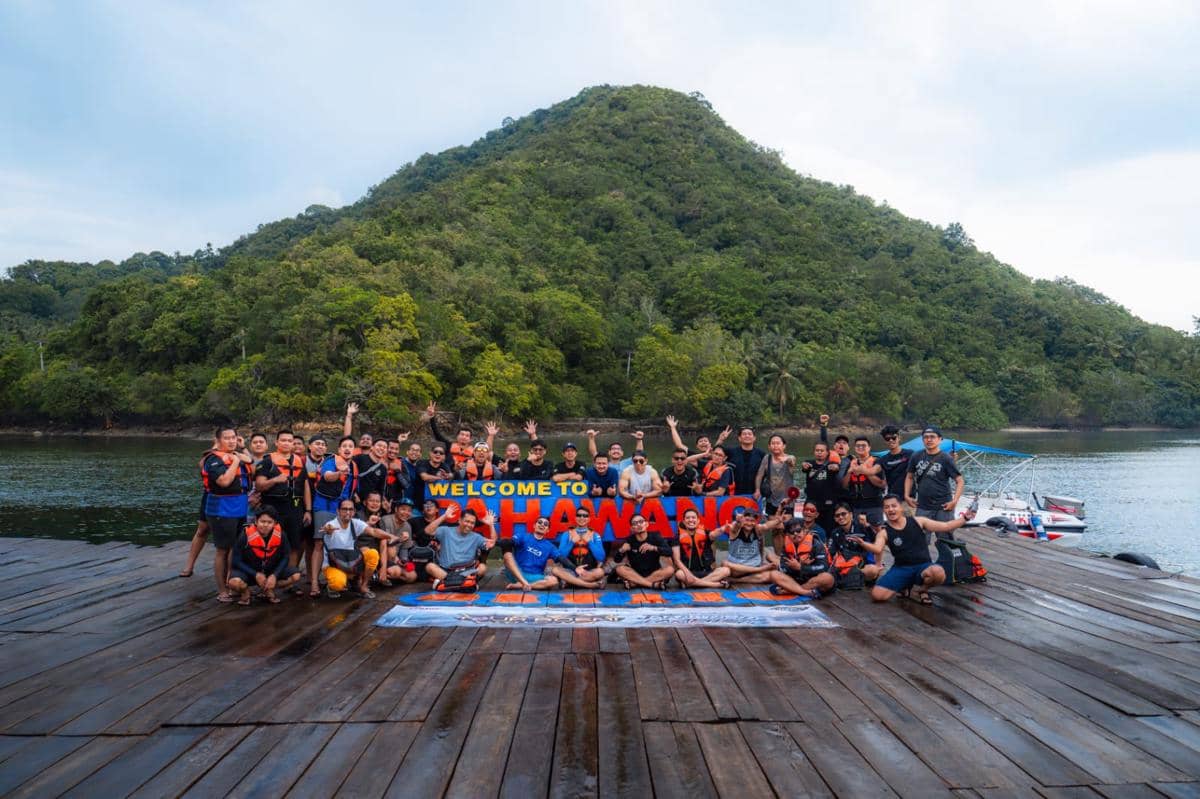 Sekelompok peserta berfoto bersama di dermaga Pulau Pahawang dengan latar perbukitan hijau dan perairan jernih.