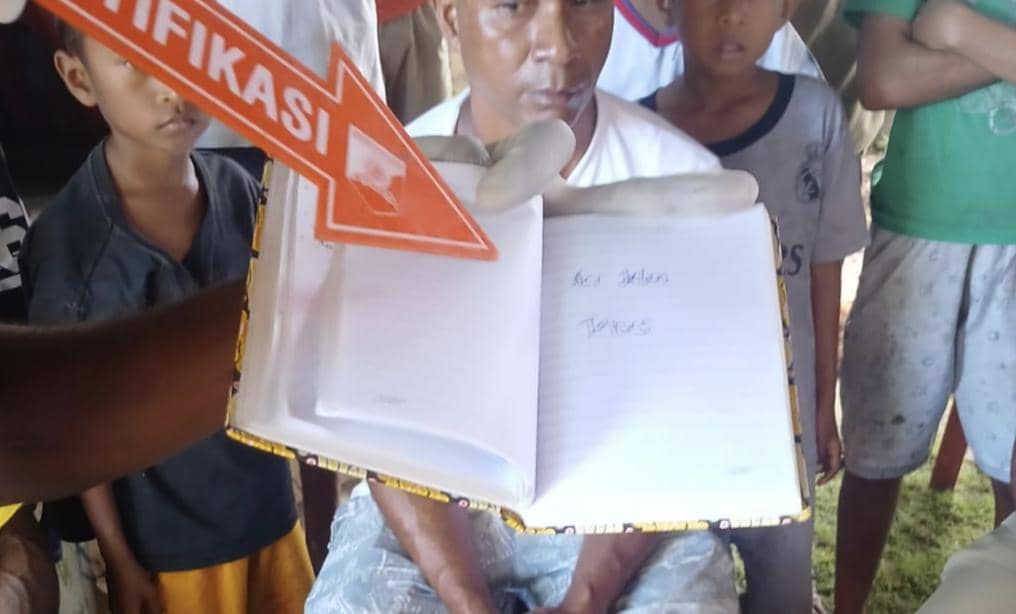 Petugas memegang buku catatan dengan tulisan tangan saat proses identifikasi di lokasi kematian seorang kepala sekolah di Lembata.