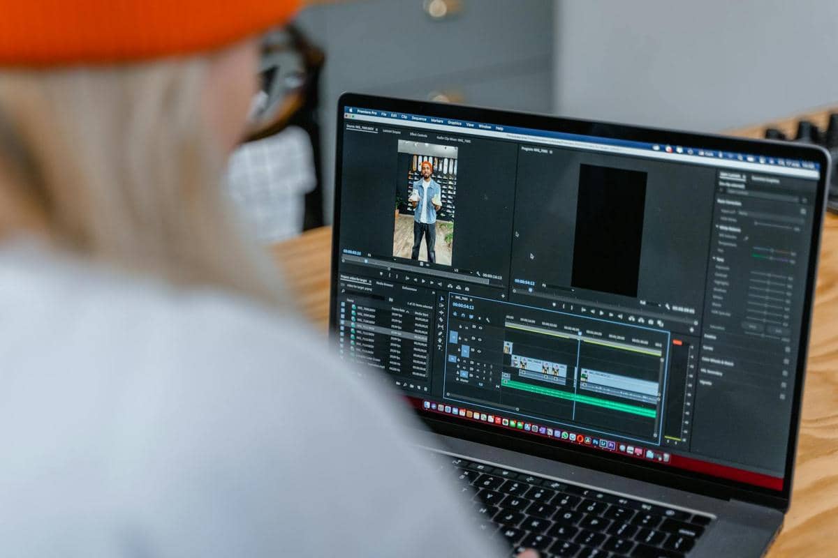 Seseorang sedang mengedit video pendek di laptop menggunakan perangkat lunak pengeditan video profesional di atas meja kayu.
