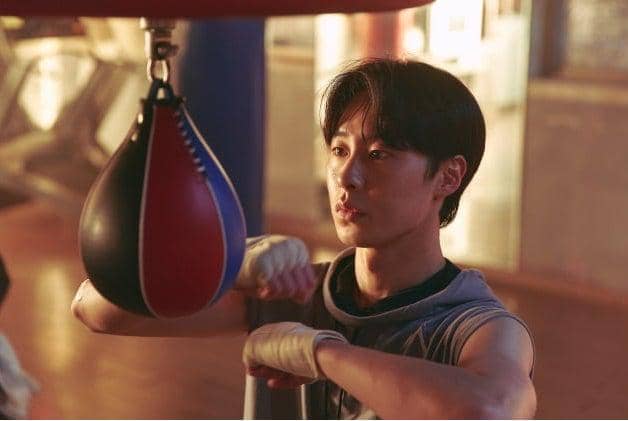 Seorang pria muda berlatih tinju dengan memukul bola kecepatan di gym, mengenakan kaus tanpa lengan dan perban di tangannya.