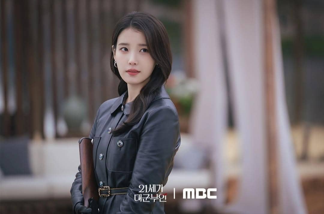 Seorang wanita berambut panjang mengenakan jaket kulit hitam memegang map cokelat dalam cuplikan drama Korea Perfect Crown.