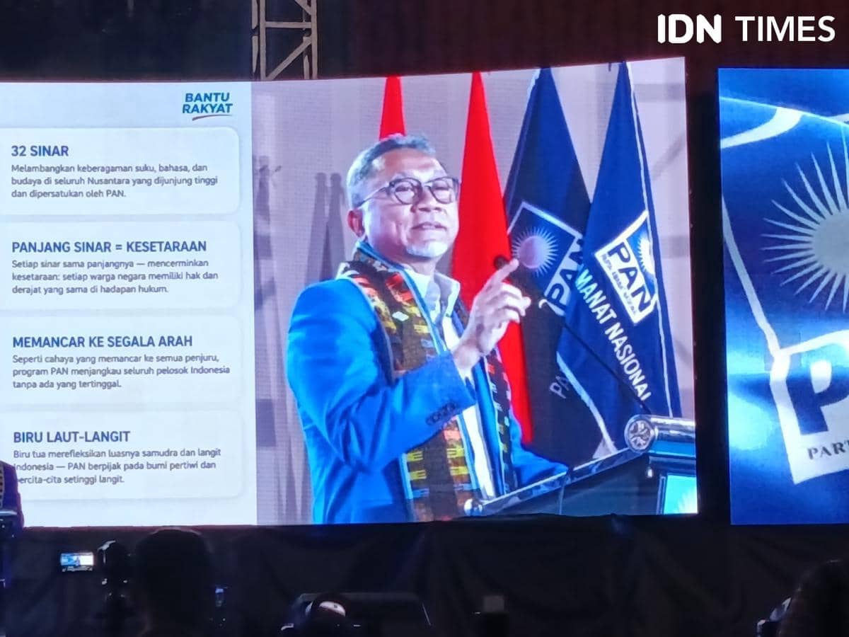 Seorang pria mengenakan jas biru berbicara di podium dengan latar layar besar berisi tulisan tentang nilai-nilai Partai Amanat Nasional di Kota Kupang.