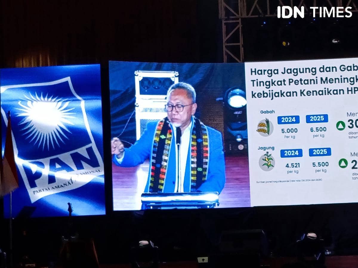 Seorang pria berjas biru berbicara di podium dengan latar belakang layar besar menampilkan logo PAN dan data harga jagung serta gabah.