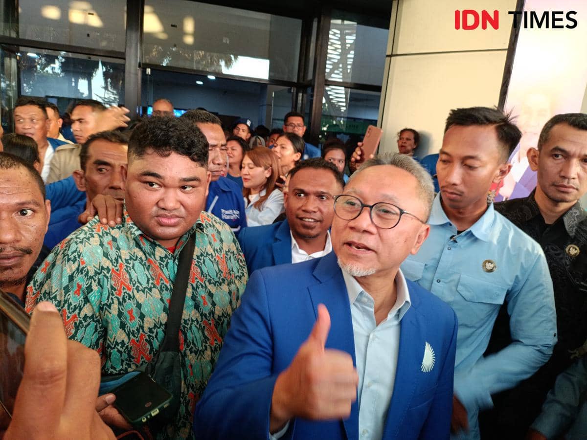 Seorang pria berjas biru memberikan acungan jempol di tengah kerumunan orang di Kota Kupang dengan suasana ramai dan antusias.