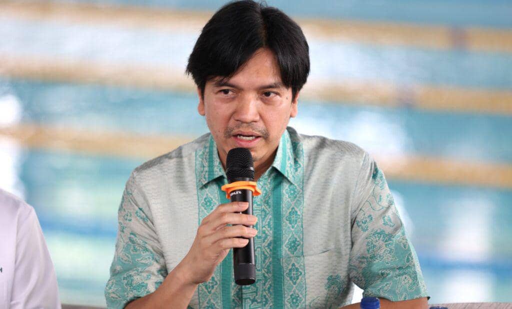 Seorang pria berbicara memegang mikrofon di depan kolam renang dalam acara persiapan Indonesia Short Course Emerging Series 2026.