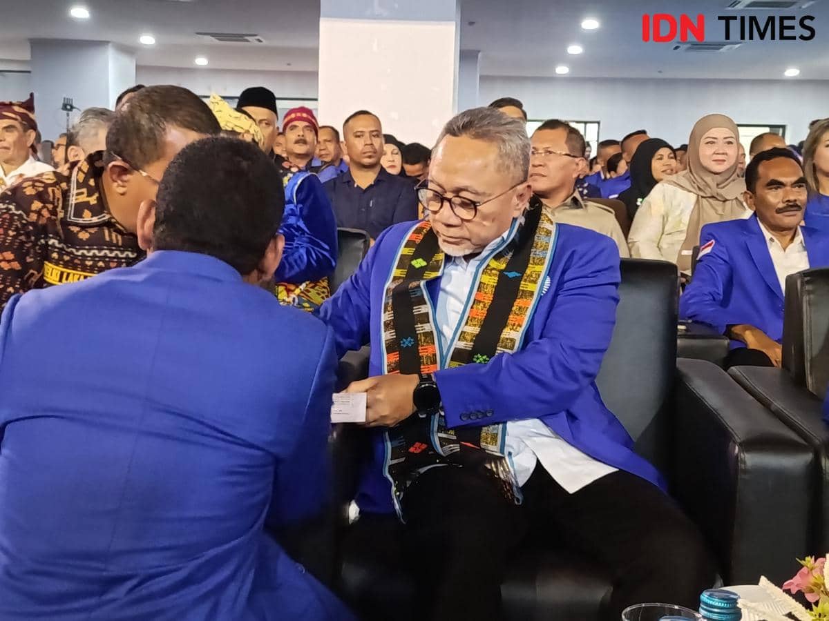 Seorang pria mengenakan jas biru dan selendang motif tenun sedang berbincang dengan peserta lain di acara partai di Kota Kupang.