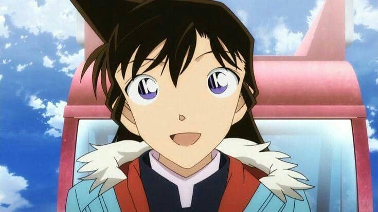 Karakter anime perempuan berambut hitam dengan mata besar tersenyum cerah di bawah langit biru berlatar wahana permainan.