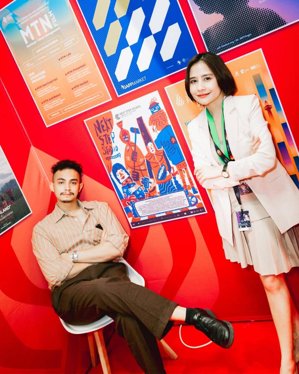 Dua orang berpose di depan dinding merah dengan poster berwarna cerah di Cannes Film Festival 2026.