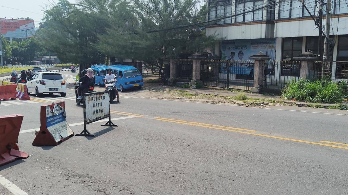 Kendaraan bermotor melintas di jalur satu arah menuju Puncak di simpang Gadog, Kabupaten Bogor, dengan rambu dan pembatas jalan terlihat di lokasi.