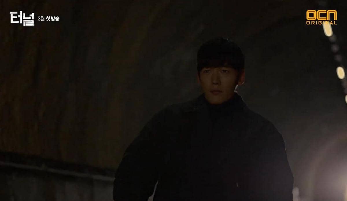 Seorang pria berdiri di dalam terowongan dengan pencahayaan redup dalam cuplikan drama Tunnel produksi OCN.
