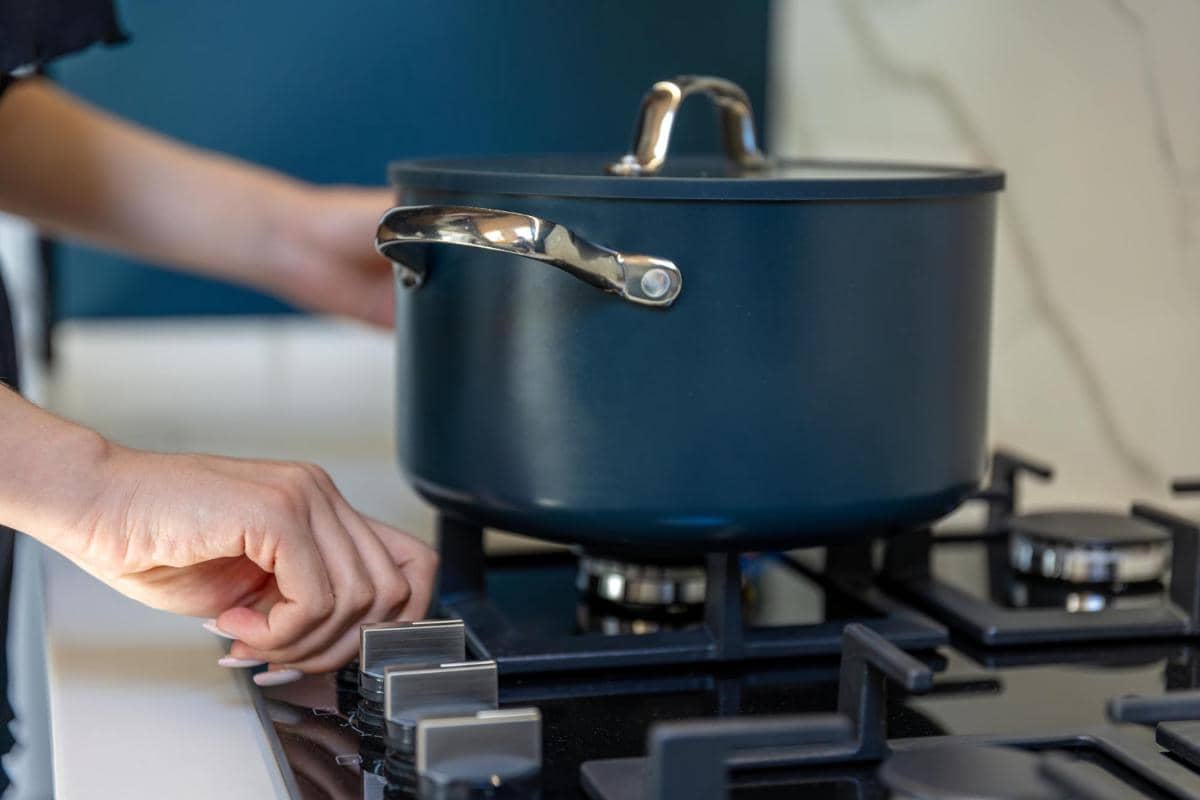 Seseorang menyalakan kompor gas dengan panci berwarna gelap di atasnya di dapur modern yang bersih dan rapi.