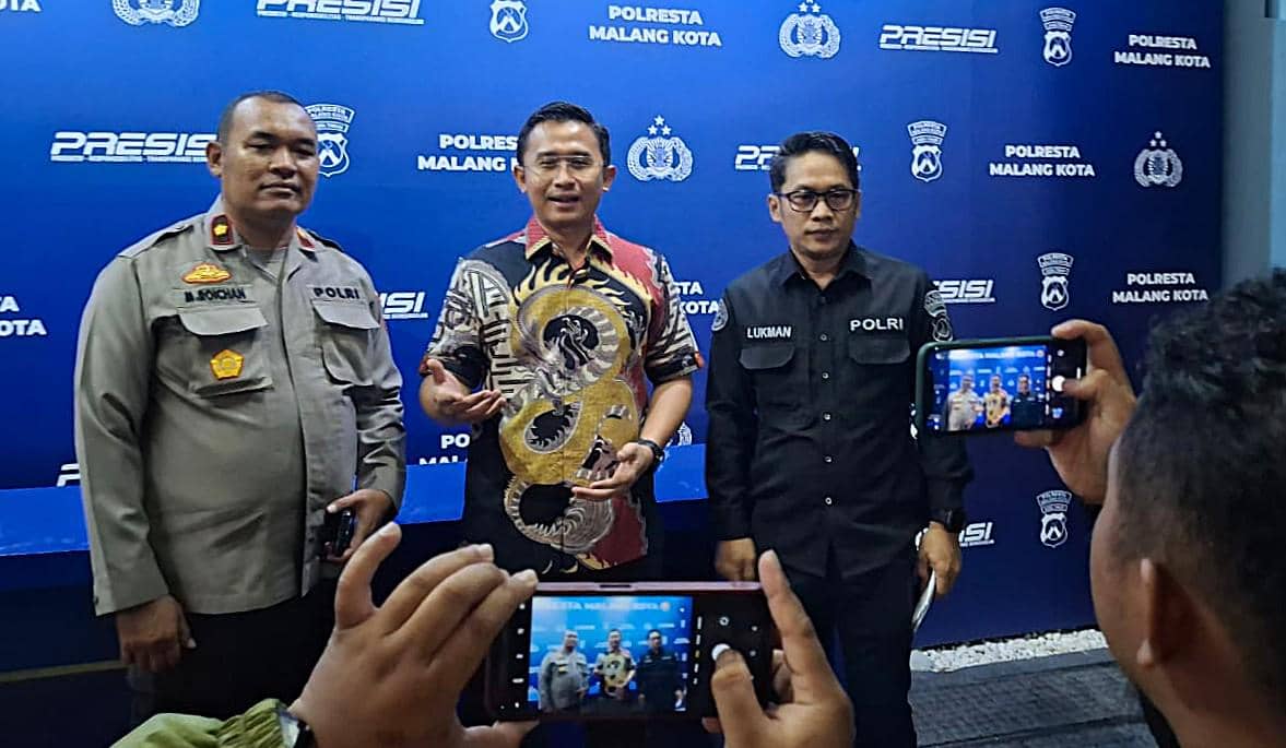 Tiga anggota kepolisian berdiri di depan latar belakang biru bertuliskan Polresta Malang Kota saat sesi foto bersama media.