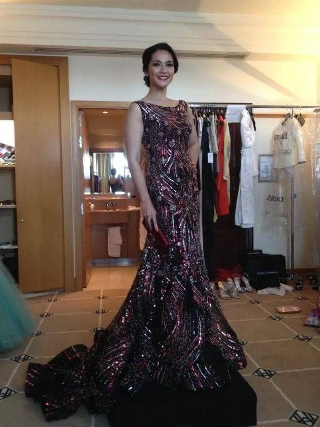 Seorang perempuan mengenakan gaun panjang berkilau warna hitam dan merah dengan detail payet di dalam ruangan berpakaian.