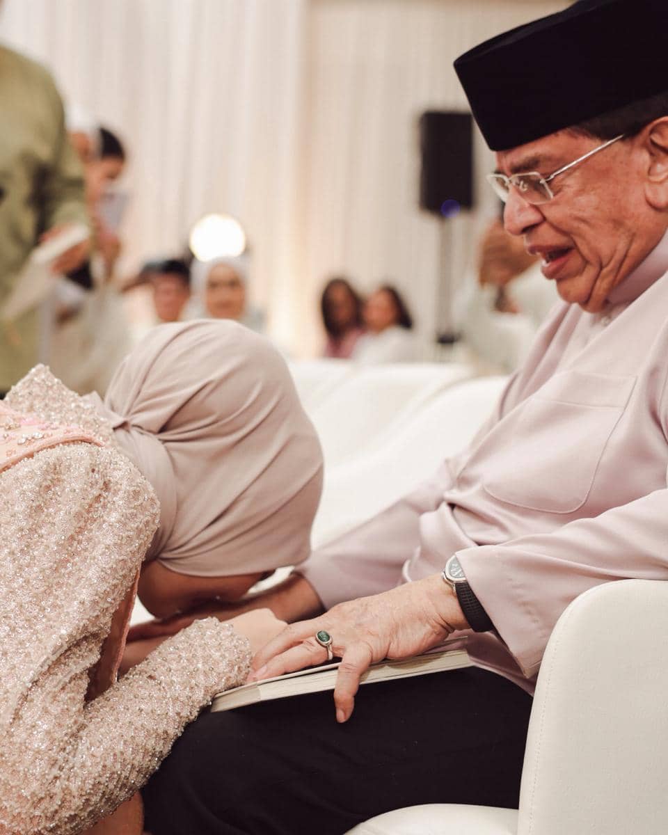 Seorang perempuan berhijab bersujud di pangkuan seorang pria lanjut usia berpakaian tradisional Melayu dalam acara pengajian pra pernikahan.