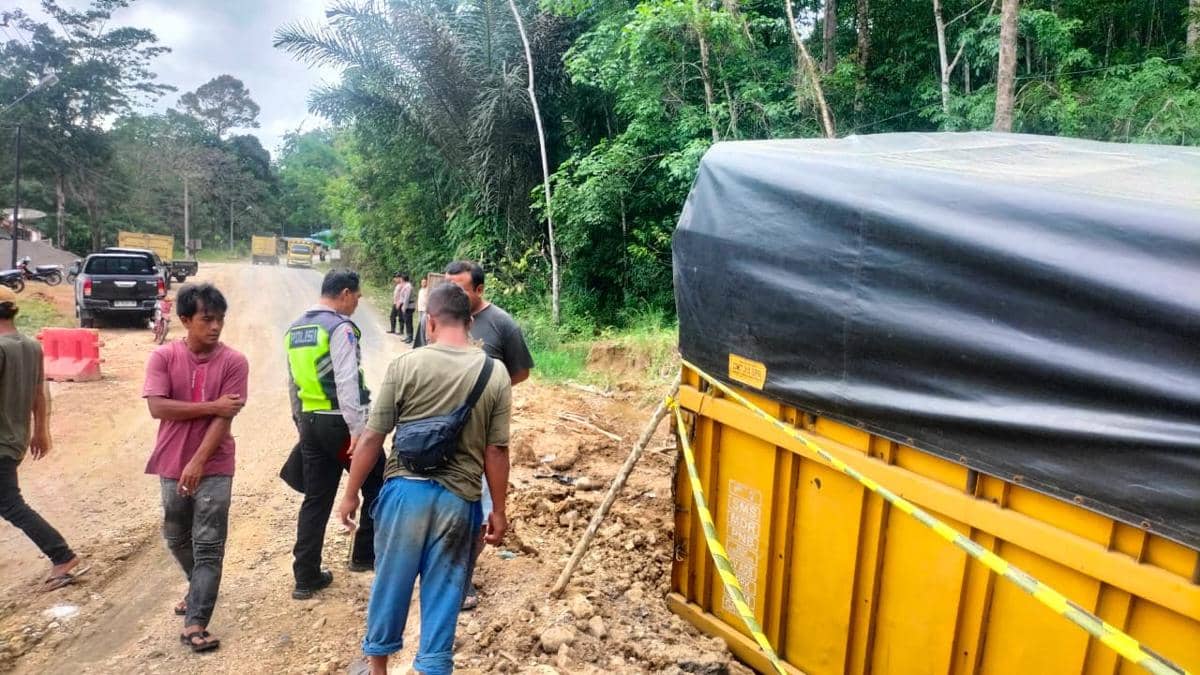 Petugas polisi dan warga memeriksa lokasi kecelakaan truk kuning yang diduga mengalami rem blong di jalan tanah dekat area hutan.