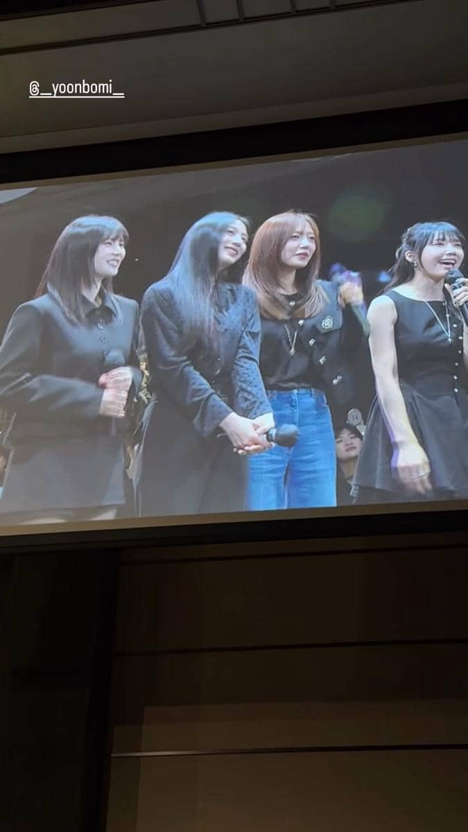 Empat wanita berdiri di atas panggung sambil memegang mikrofon dan tersenyum dalam acara pernikahan Bomi Apink dan Rado.
