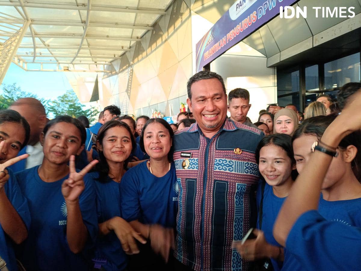 Seorang pria mengenakan kemeja bermotif tenun berfoto bersama sekelompok remaja perempuan berbaju biru di sebuah acara di Kupang.