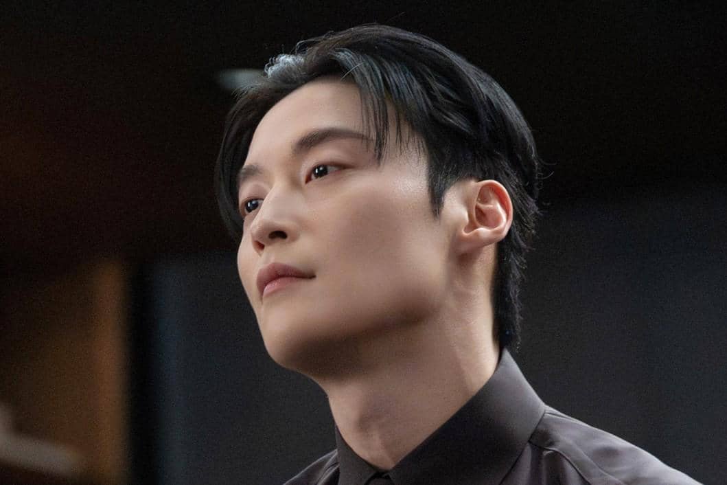 Seorang pria berpenampilan rapi dengan kemeja gelap menatap ke arah samping dalam adegan drama My Royal Nemesis.