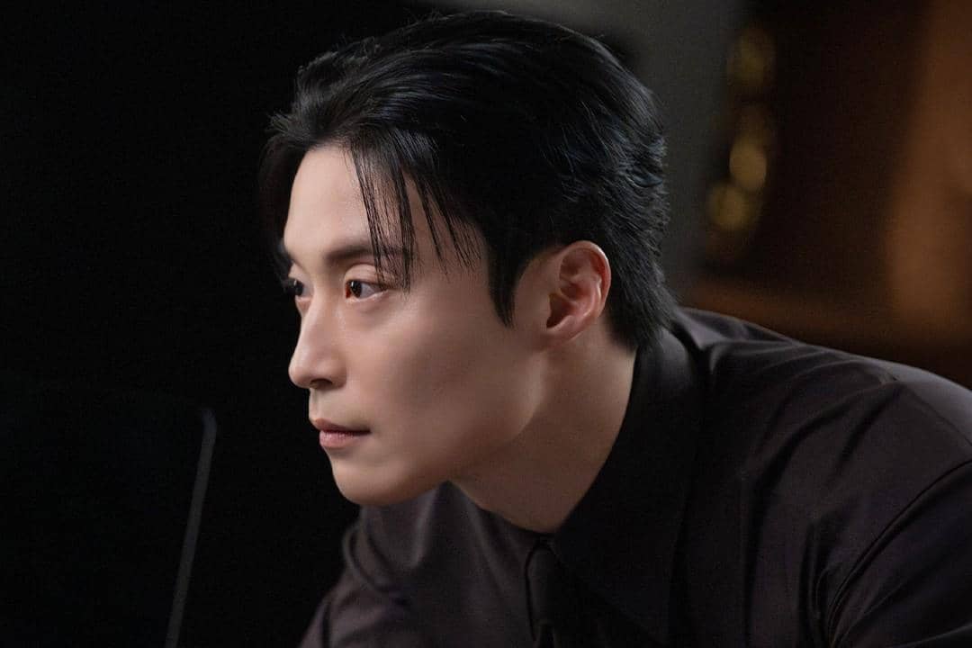Seorang pria berambut hitam mengenakan kemeja gelap menatap serius ke arah samping dalam adegan drama My Royal Nemesis.