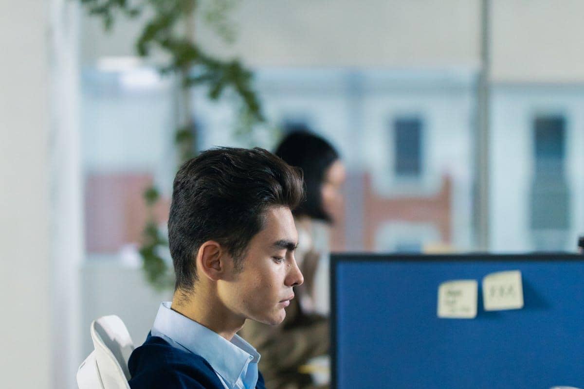 Seorang pria duduk di kursi kantor dengan mata terpejam, tampak fokus melakukan teknik pernapasan di ruang kerja modern.