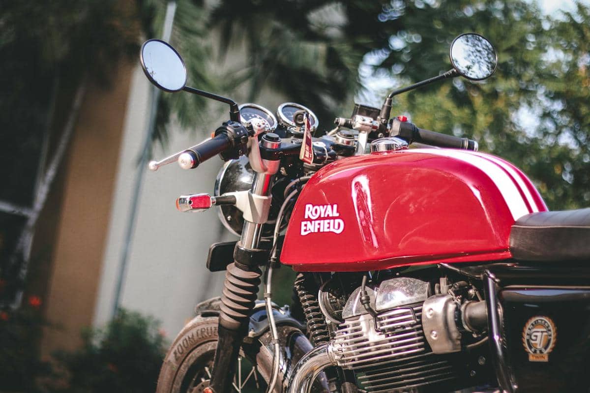Motor retro modern berwarna merah dengan tangki bahan bakar bergaris putih dan detail krom, diparkir di luar ruangan.