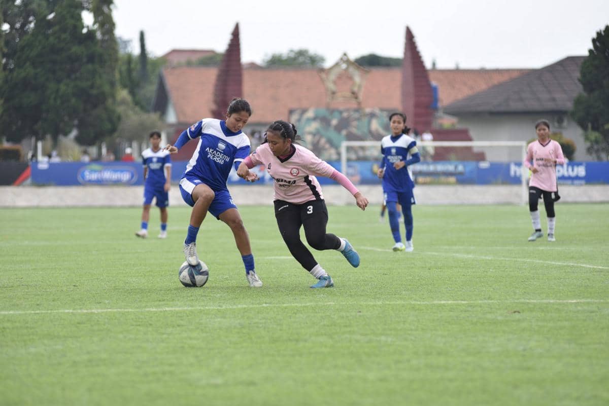 Pemain sepak bola wanita dari dua tim berseragam biru dan merah muda berebut bola di lapangan dalam ajang Hydroplus Soccer League Bandung.