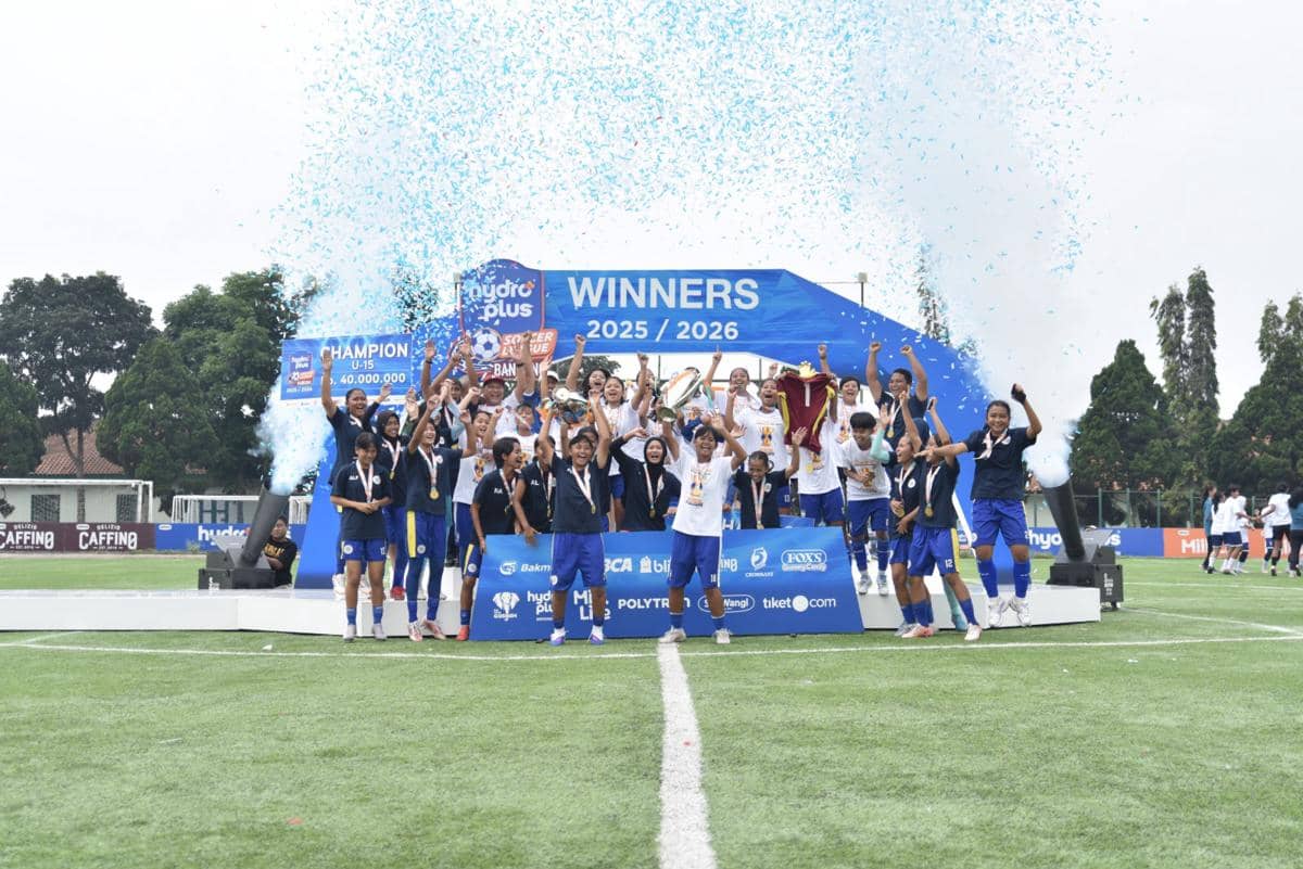 Tim sepak bola muda merayakan kemenangan di panggung juara Hydroplus Soccer League Bandung 2025/2026 dengan konfeti biru di udara.