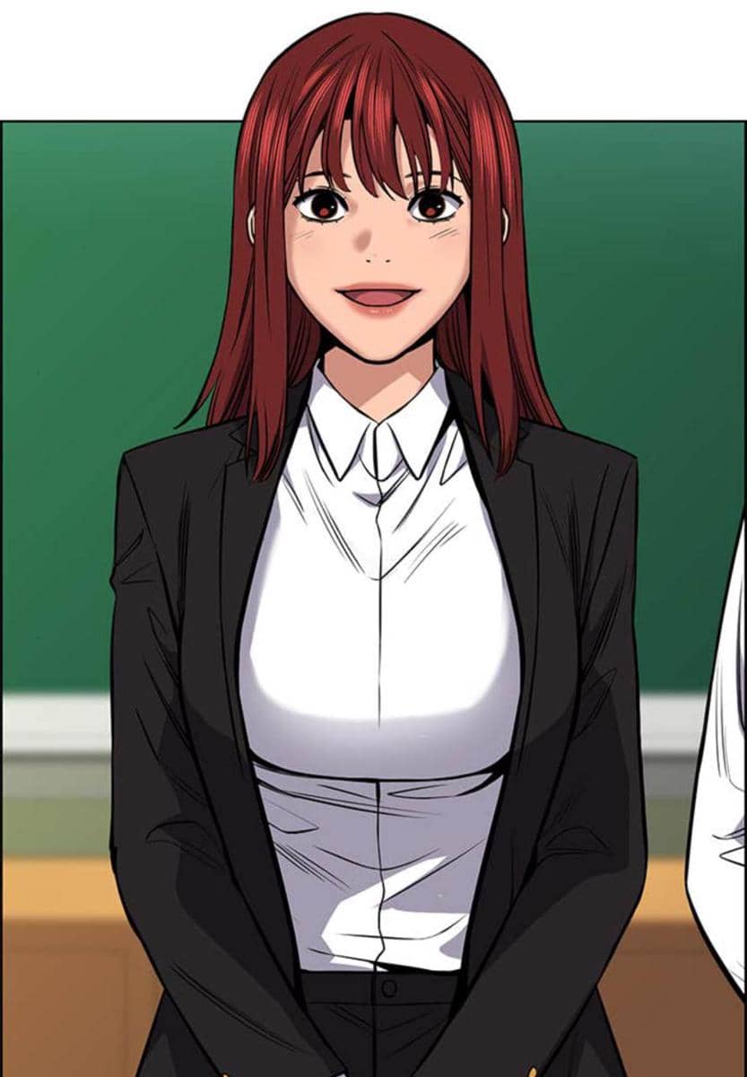 Karakter perempuan berambut merah mengenakan kemeja putih dan jas hitam berdiri di depan papan tulis dalam webtoon Teach You a Lesson.