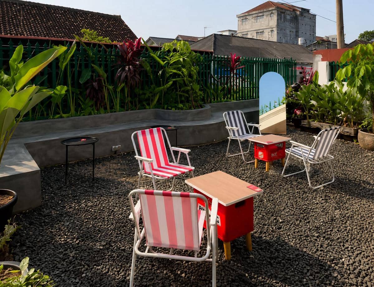 Area outdoor Distrik15 di Kota Metro dengan kursi bergaris merah putih bergaya retro, meja kecil, dan tanaman hijau di sekitarnya.