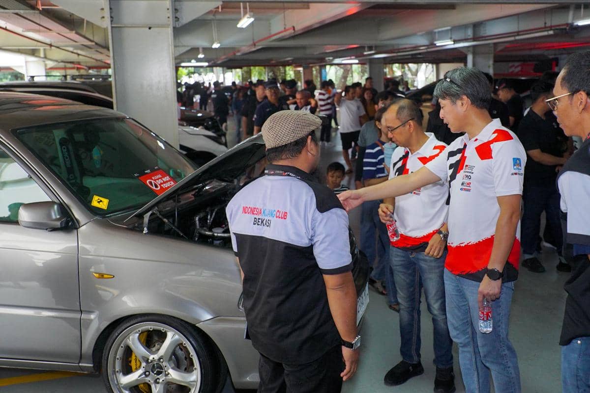 Beberapa anggota komunitas mobil Toyota berbincang di area parkir sambil melihat mobil dengan kap mesin terbuka.
