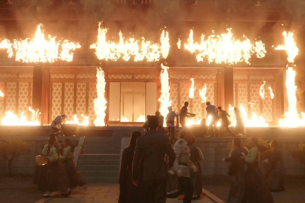 Bangunan bergaya tradisional Korea terbakar hebat dengan api besar, sementara sekelompok orang berlari panik menjauh dari kobaran api.