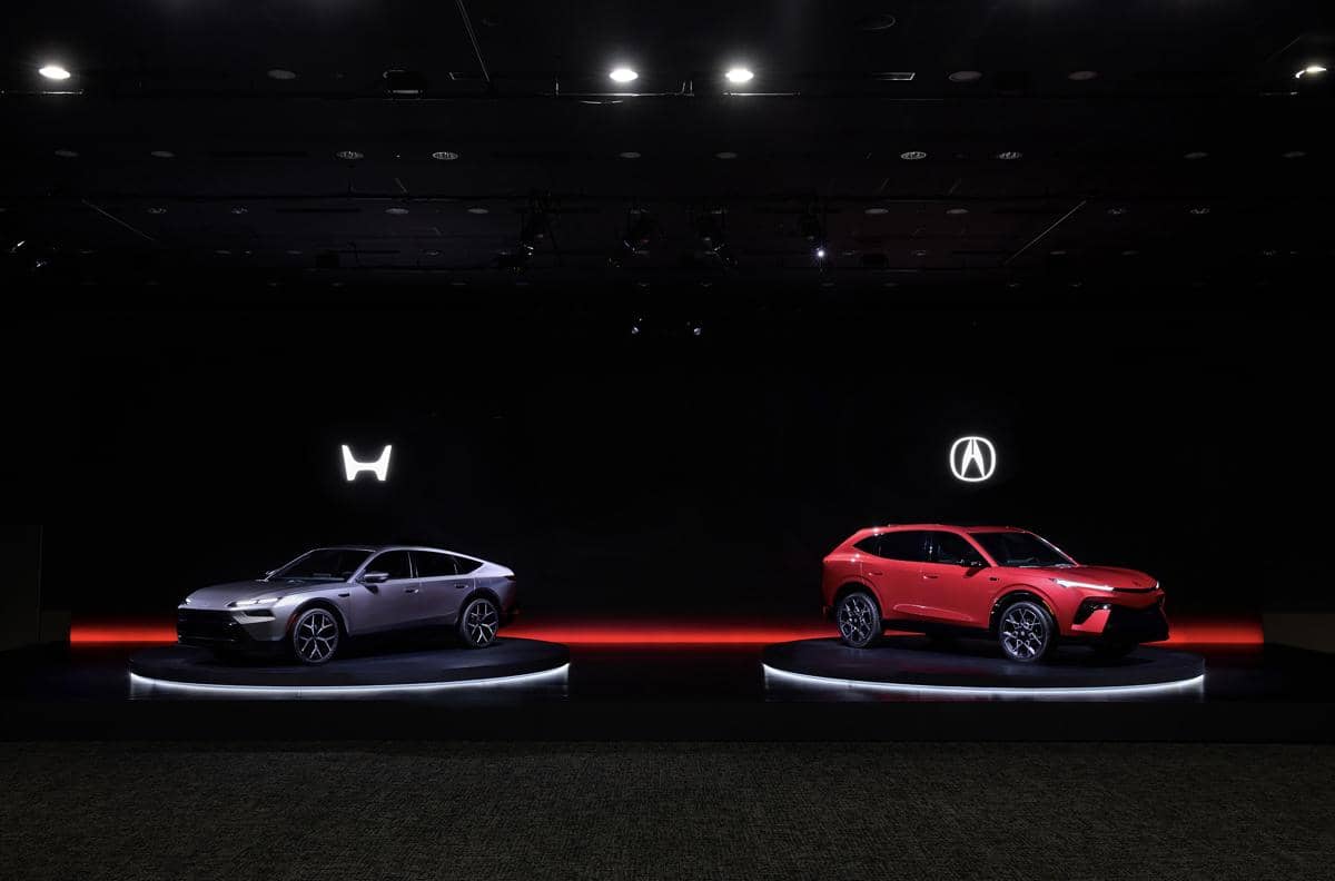 Dua mobil prototipe baru Honda dipamerkan di atas panggung dengan pencahayaan gelap, satu berwarna abu-abu dan satu berwarna merah.