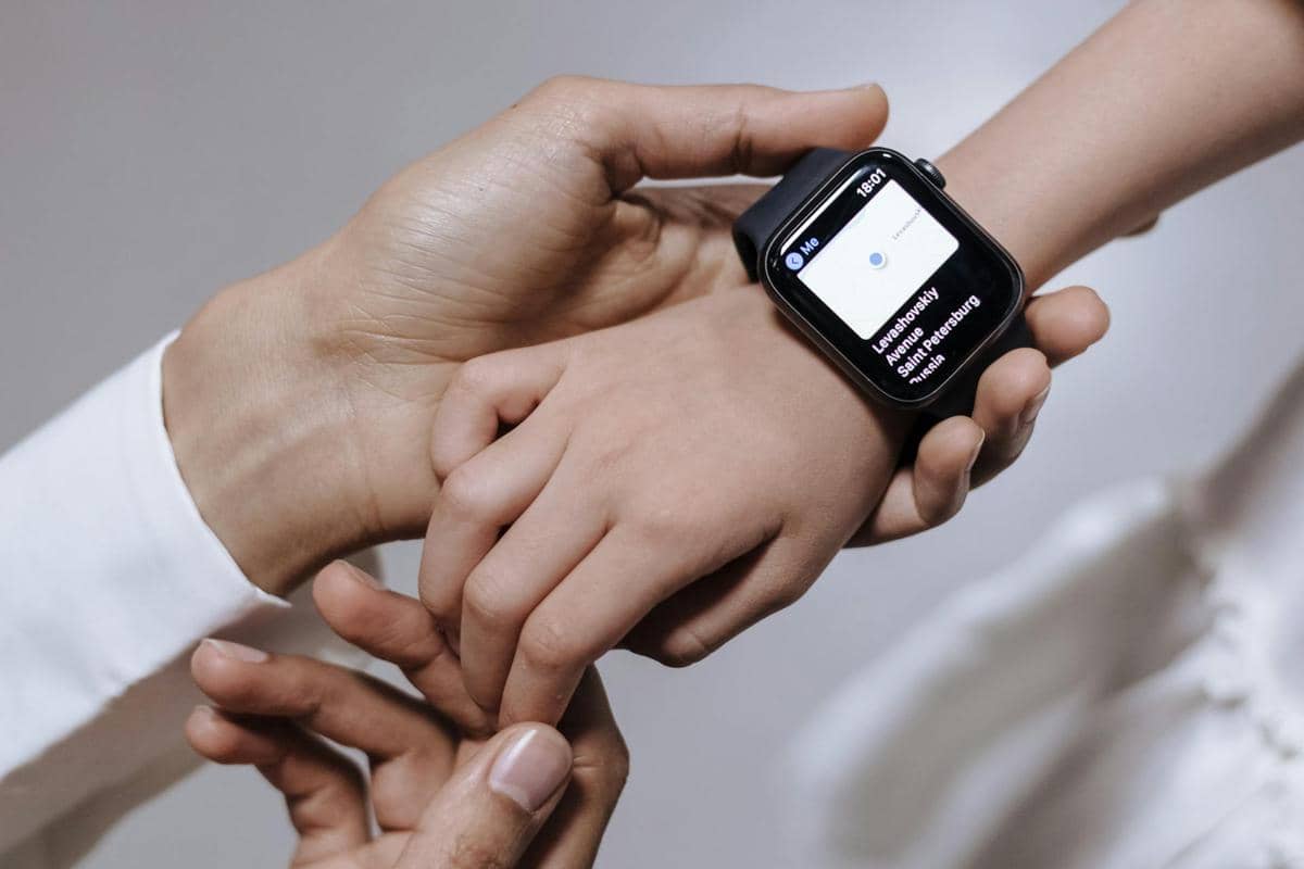 Seorang anak mengenakan smartwatch hitam di pergelangan tangan sementara orang dewasa memegang tangannya dengan lembut.