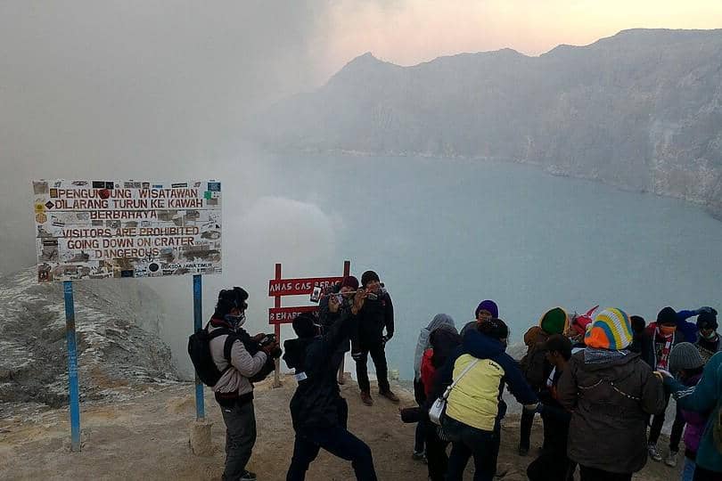 Ilustrasi wisatawan menikmati panorama Kawah Ijen saat sunrise dengan latar danau kawah yang berkabut.