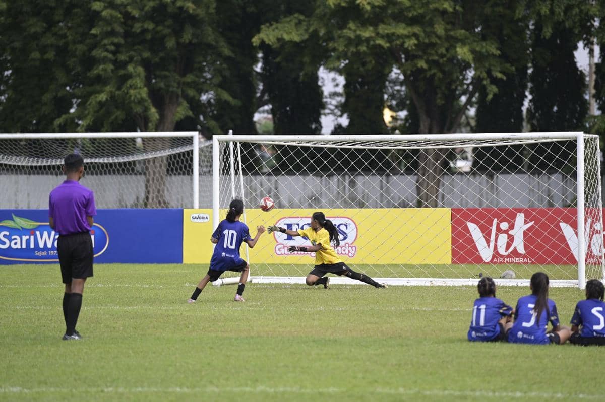 Pemain sepak bola muda menendang bola ke arah gawang saat kiper berusaha menepis dalam pertandingan MLSC Surabaya Seri 2 2025-2026.