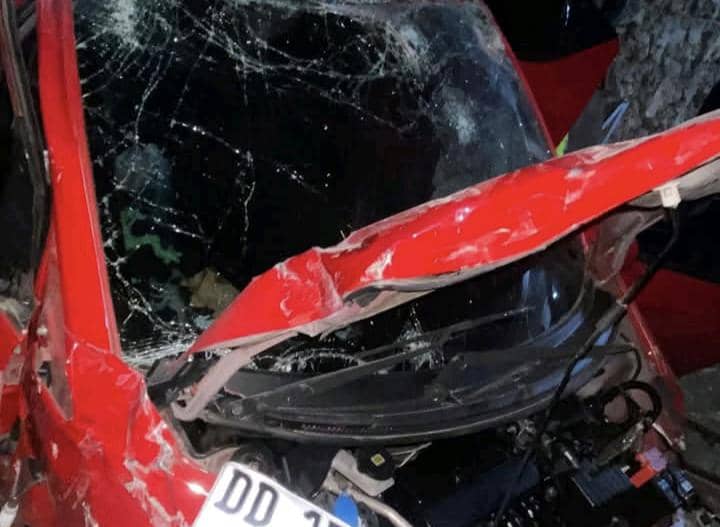Mobil berwarna merah mengalami kerusakan parah dengan kaca depan pecah dan bodi depan ringsek akibat kecelakaan di Kupang.