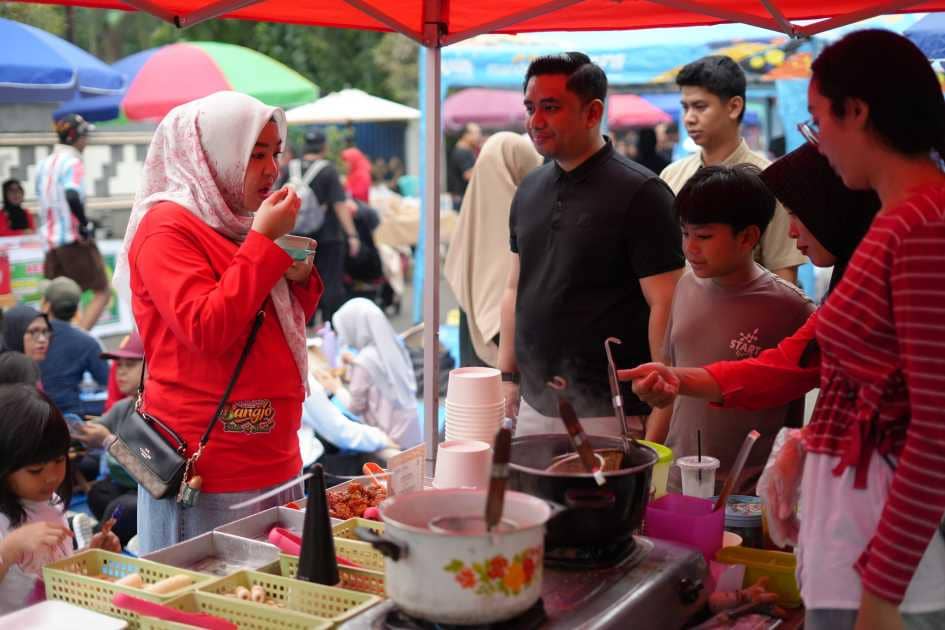 Pengunjung menikmati makanan di stan kuliner UMKM Street Bangjo Kota Metro dengan suasana ramai di bawah tenda berwarna merah.