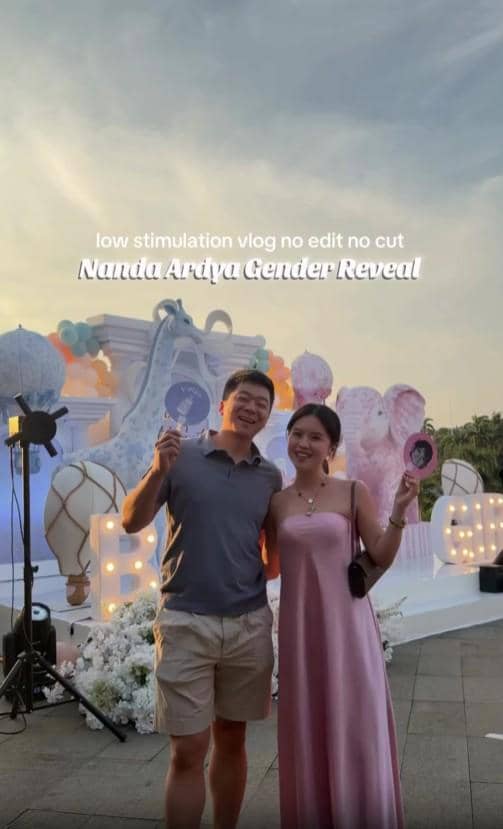 Seorang pria dan wanita berpose bersama di acara gender reveal Nanda Arsyinta dengan dekorasi balon dan lampu di latar belakang.