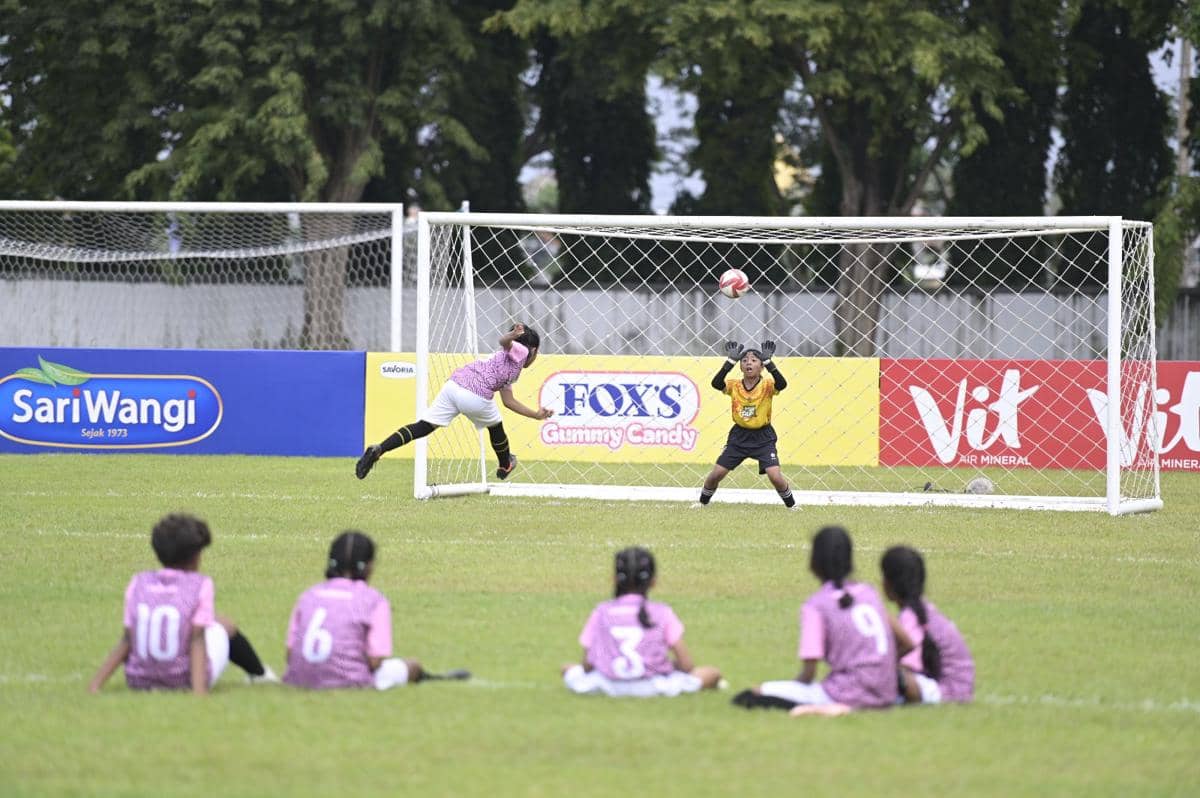 Pemain muda menendang bola ke arah gawang saat pertandingan sepak bola MLSC Surabaya Seri 2 2025-2026 dengan penjaga gawang bersiap menahan bola.