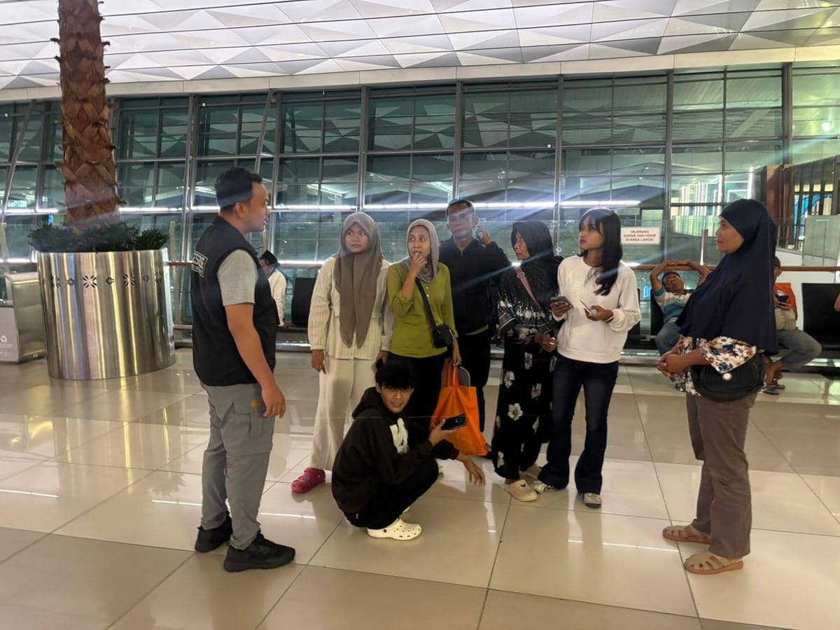 Petugas berbicara dengan sekelompok calon jemaah haji di area keberangkatan Bandara Soekarno-Hatta dengan latar terminal modern.
