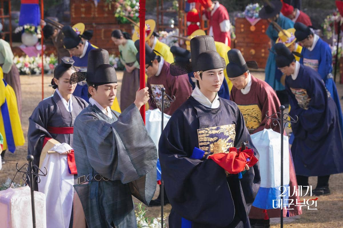 Para aktor mengenakan hanbok tradisional Korea dalam adegan upacara kerajaan dari drama Korea Perfect Crown di luar ruangan.