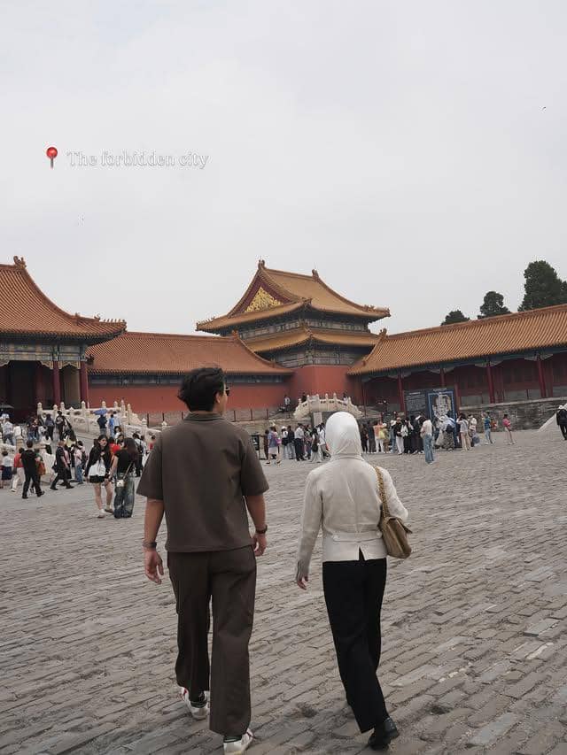 Dua orang berjalan di area Kota Terlarang Beijing dengan latar bangunan berarsitektur tradisional Tiongkok dan pengunjung lainnya.